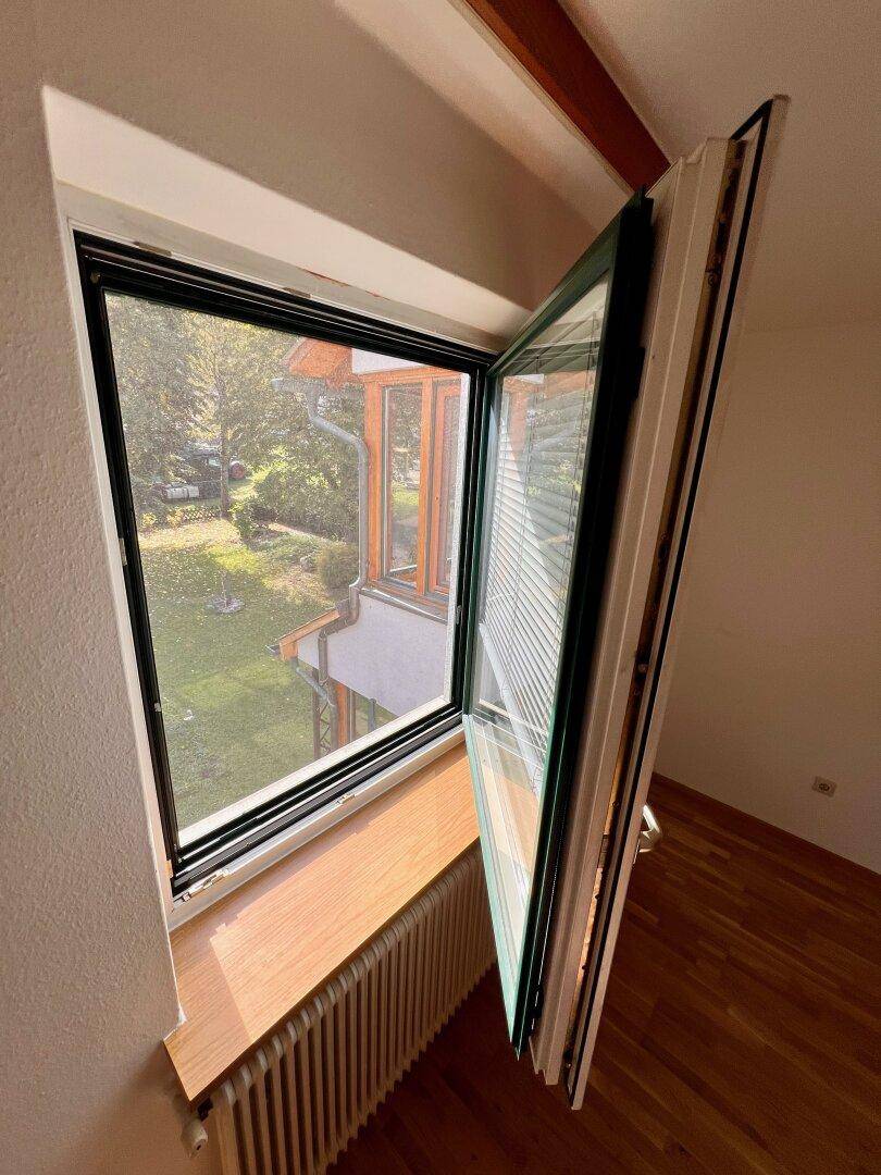 Geöffnetes Fenster mit Blick auf den grünen Garten und die umliegende Natur.