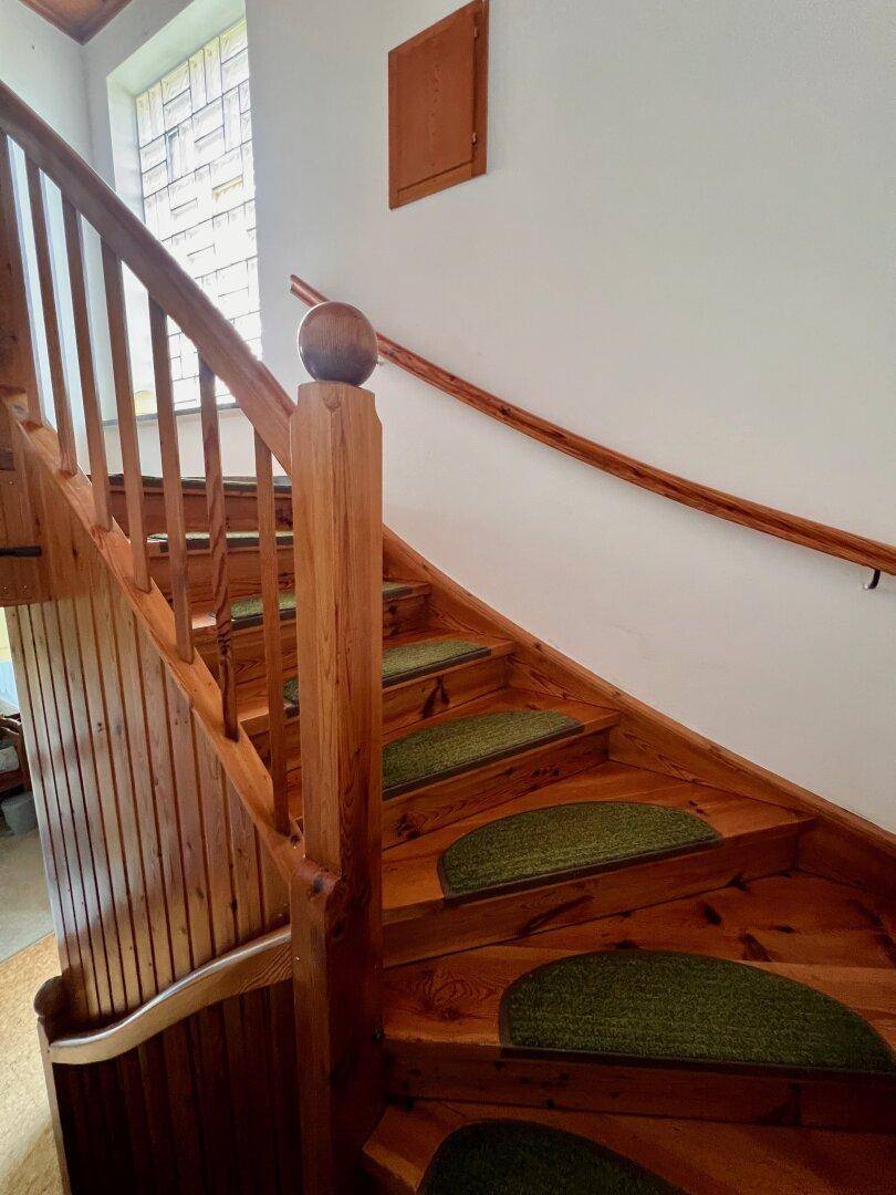 Rustikale Holztreppe mit Teppichstufen und Holzgeländer, die die Stockwerke verbindet.