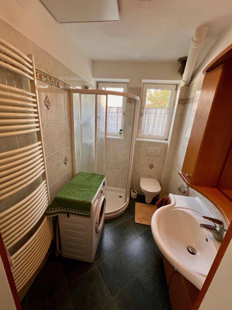 Badezimmer mit Dusche, Waschbecken, Toilette, Waschmaschine und beheiztem Handtuchhalter.