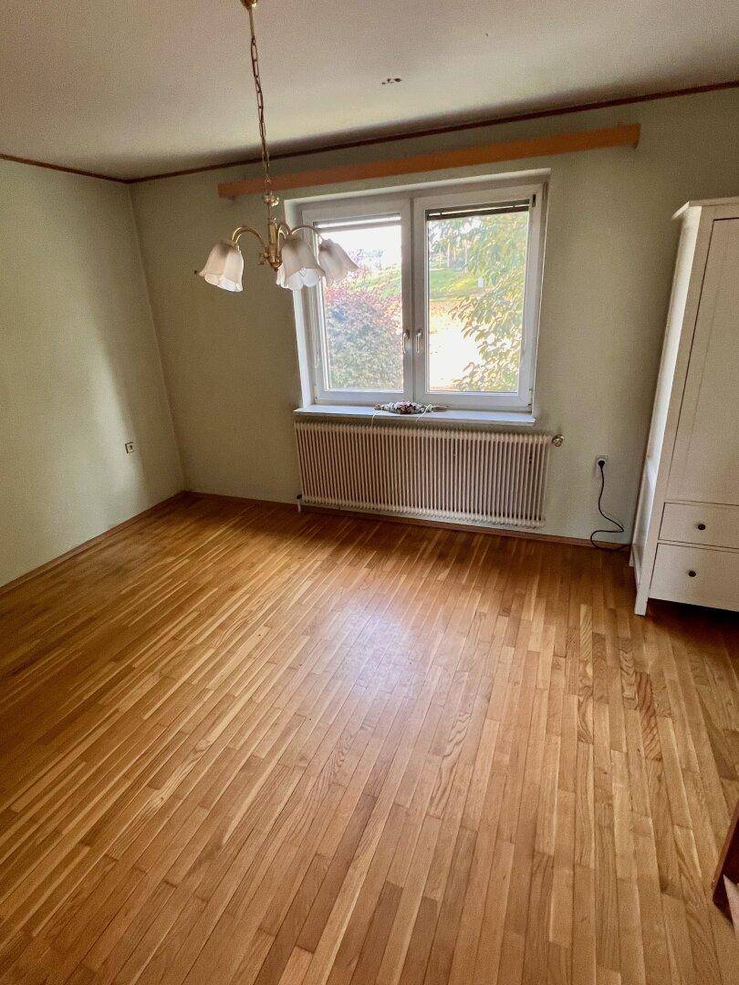 Helles Schlafzimmer mit Holzboden, einem Fenster und einem Heizkörper unter dem Fenster.