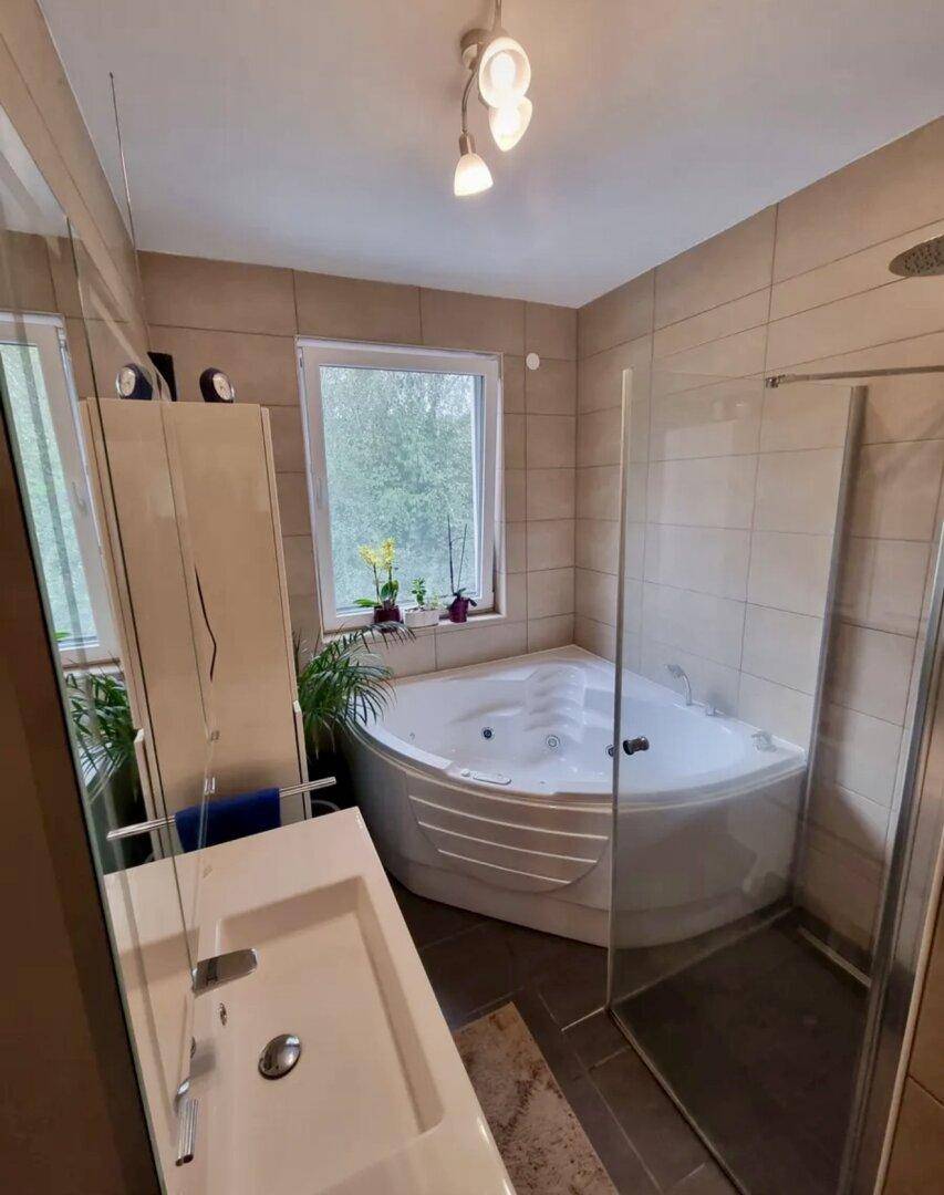Modernes Badezimmer mit Eck-Whirlpool, Dusche und Fenster für natürliches Licht.
