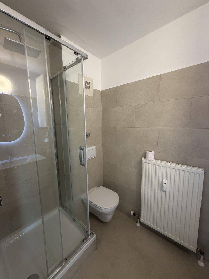 Helles Badezimmer mit Duschkabine, wandhängendem WC und Heizkörper.