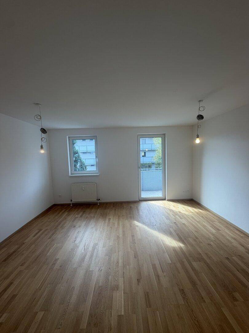 Geräumiges Zimmer mit hellem Parkettboden, Fenster und Zugang zum Balkon.
