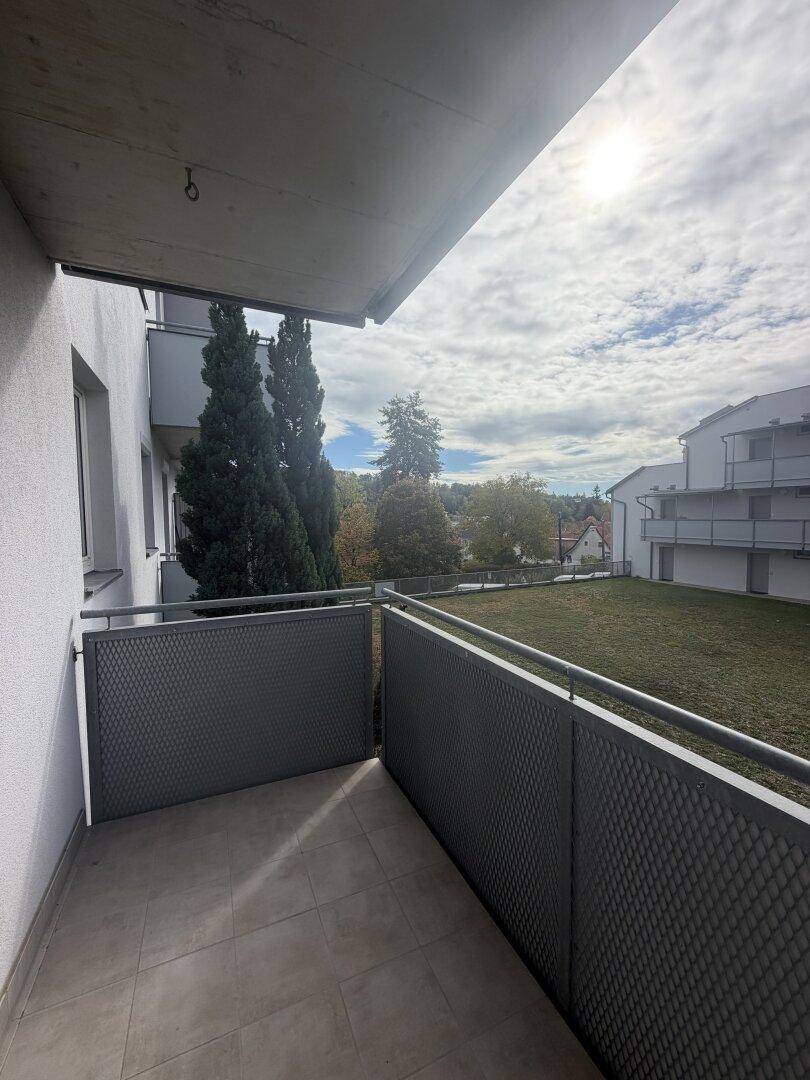 Balkon mit Fliesenboden und Blick auf die grüne Umgebung und andere Gebäude.