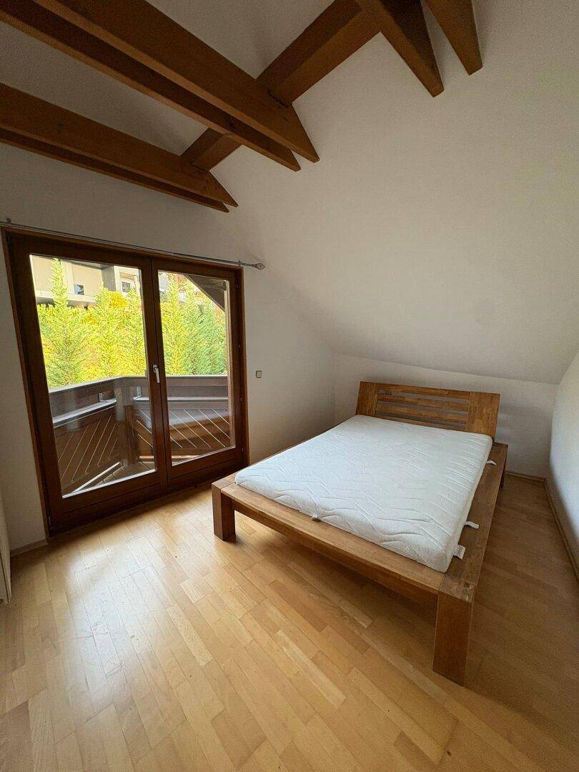Gemütliches Schlafzimmer im Dachgeschoss mit Holzbett, Parkettboden und direktem Zugang zum Balkon.