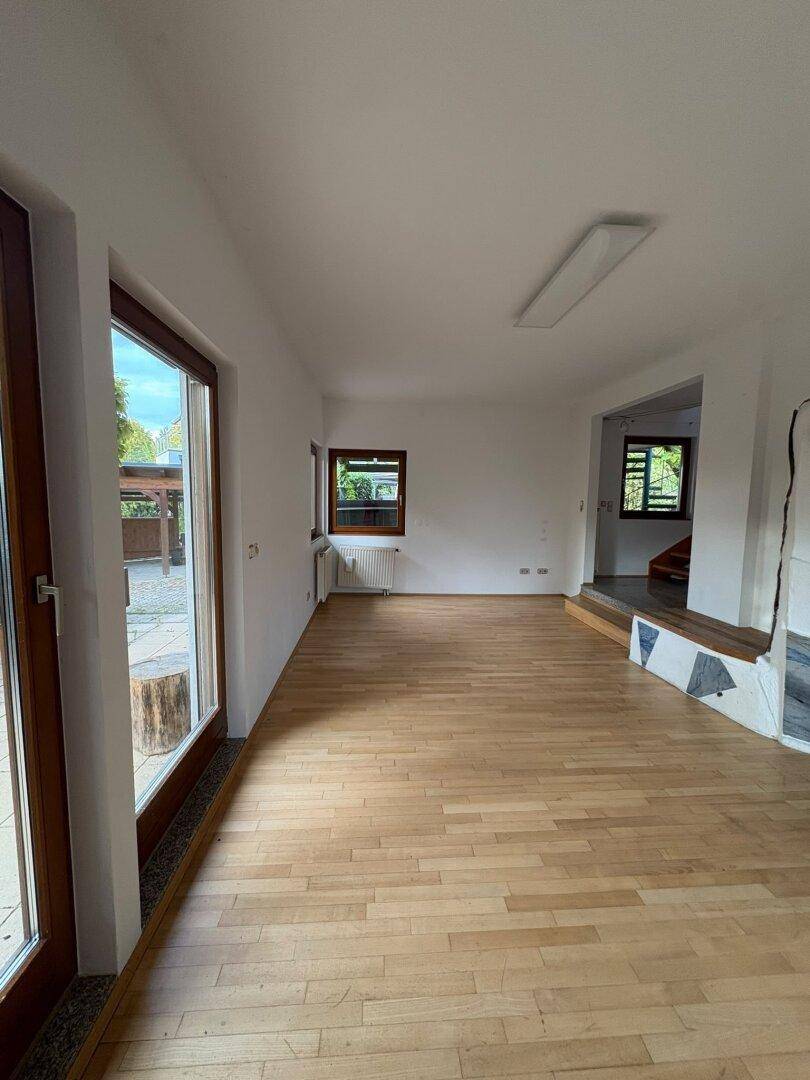 Helles Wohnzimmer mit Holzboden und großen Fenstern, die viel Tageslicht hereinlassen.
