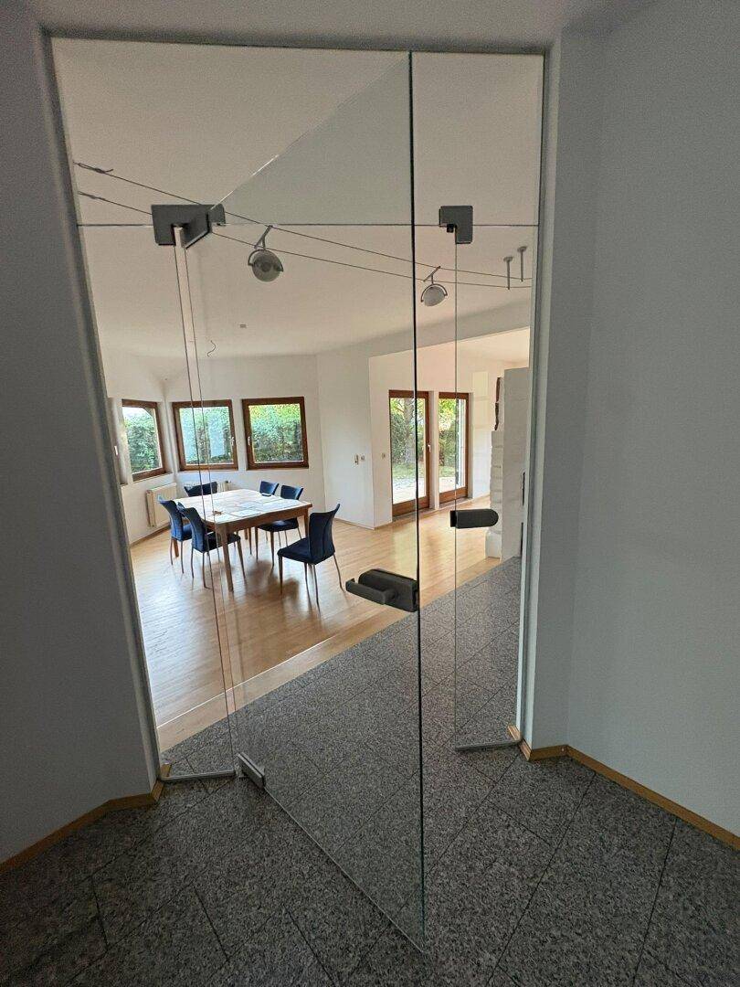 Blick durch Glastüren in einen hellen Essbereich mit Holzboden und einem großen Esstisch.
