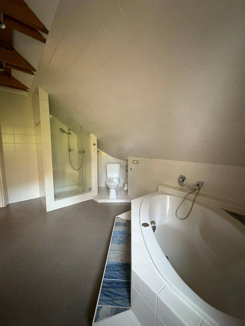 Geräumiges Badezimmer im Dachgeschoss mit Badewanne, Duschkabine und Fliesenboden unter Dachschrägen.