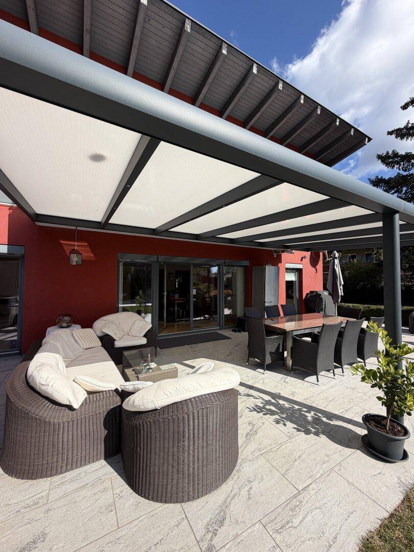 Großzügige überdachte Terrasse mit bequemen Lounge-Möbeln und Essbereich am roten Haus.
