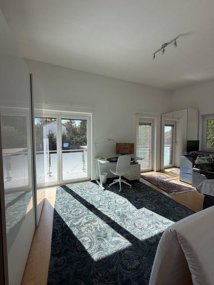 Helles Schlafzimmer mit Schreibtisch und direktem Zugang zu einem sonnigen Balkon.