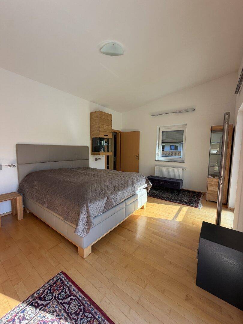 Helles Schlafzimmer mit großem Bett, Holzmöbeln und einem Fenster mit Blick ins Grüne.
