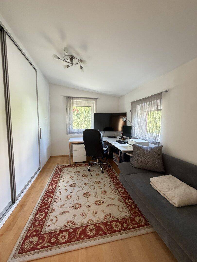 Funktionales Büro mit großem Schreibtisch, bequemer Couch und integriertem Kleiderschrank.