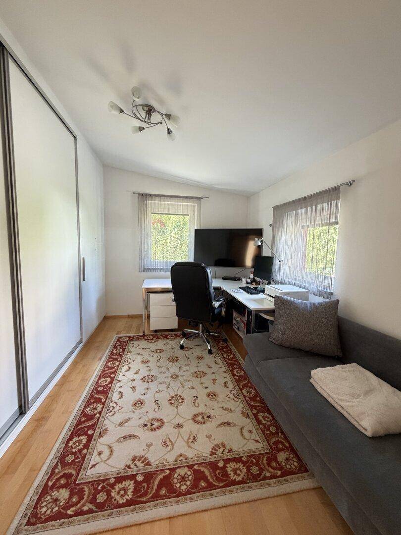 Helles Arbeitszimmer mit Schreibtisch, Sofa und praktischen Einbauschränken.