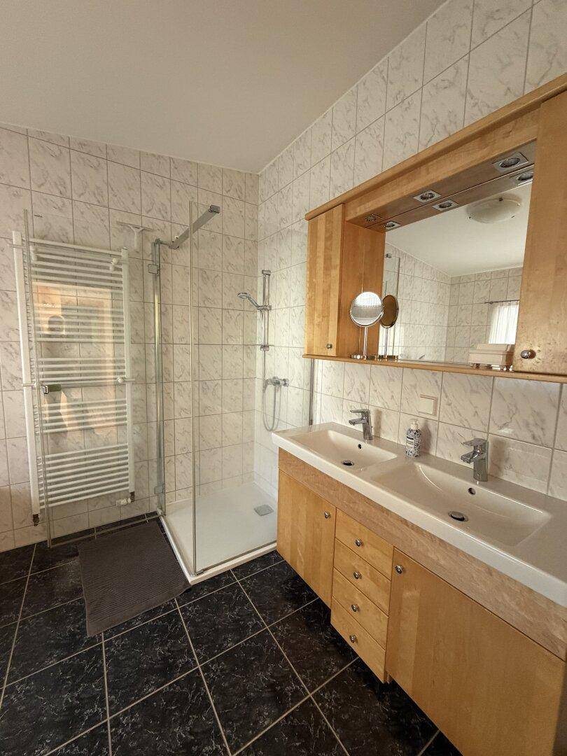 Modernes Badezimmer mit Duschkabine, Doppelwaschbecken und beheiztem Handtuchhalter.