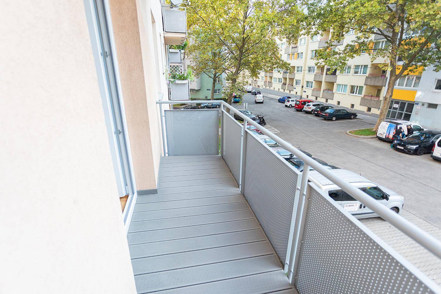 Moderner Balkon mit grauem Bodenbelag und perforiertem Geländer, mit Blick auf die Straße.
