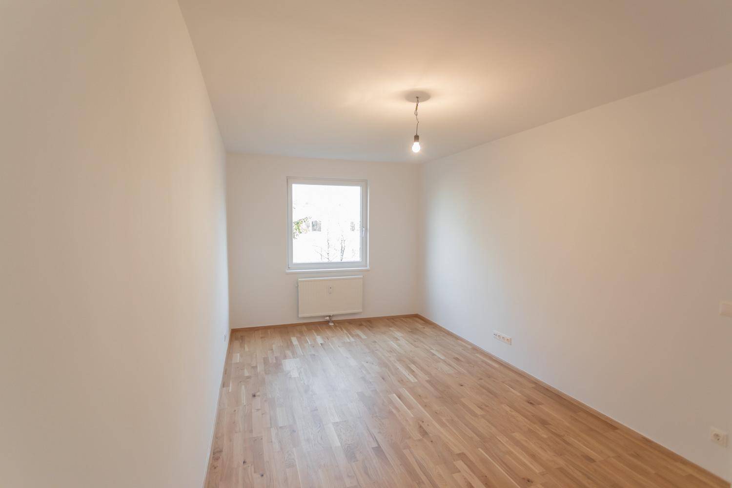 Leerer Raum mit hellem Parkettboden und einem Fenster, bereit zur individuellen Gestaltung.