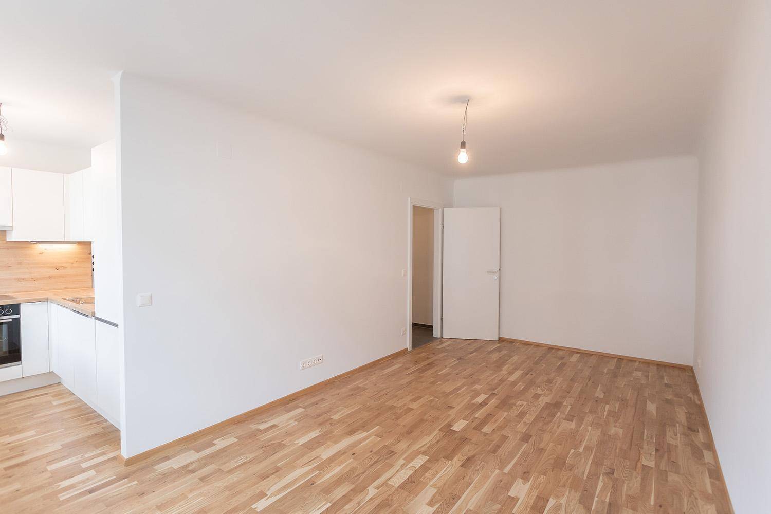 Geräumiger Wohnbereich mit hellem Parkettboden und weiß gestrichenen Wänden, unmöbliert und hell.