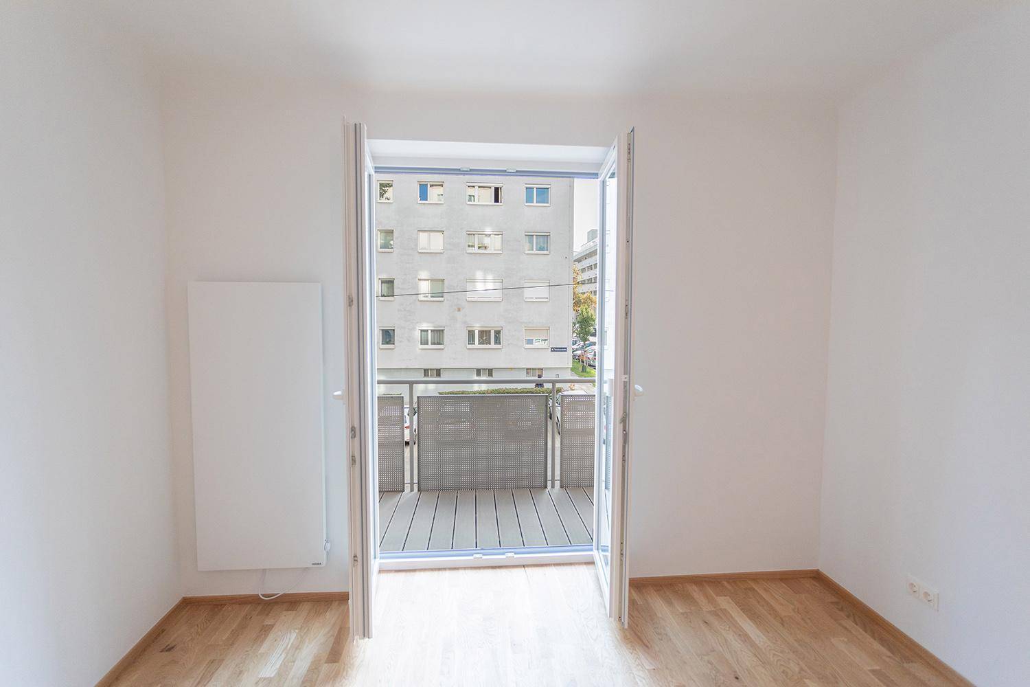 Heller Raum mit Zugang zu einem Balkon und Blick auf die umliegenden Gebäude.