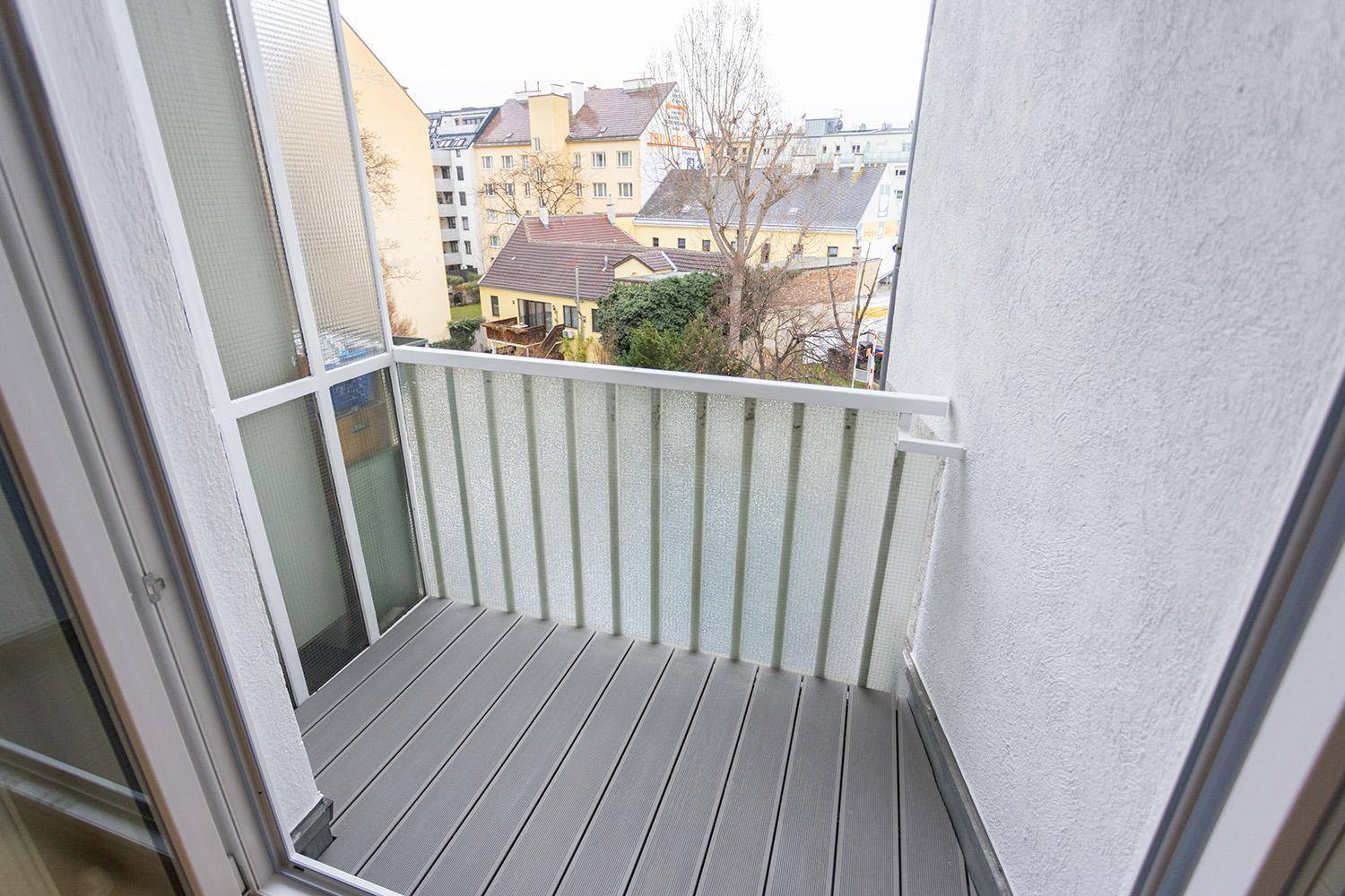 Kleiner Balkon mit Holzdielen und Blick auf die umliegenden Gebäude und Bäume.