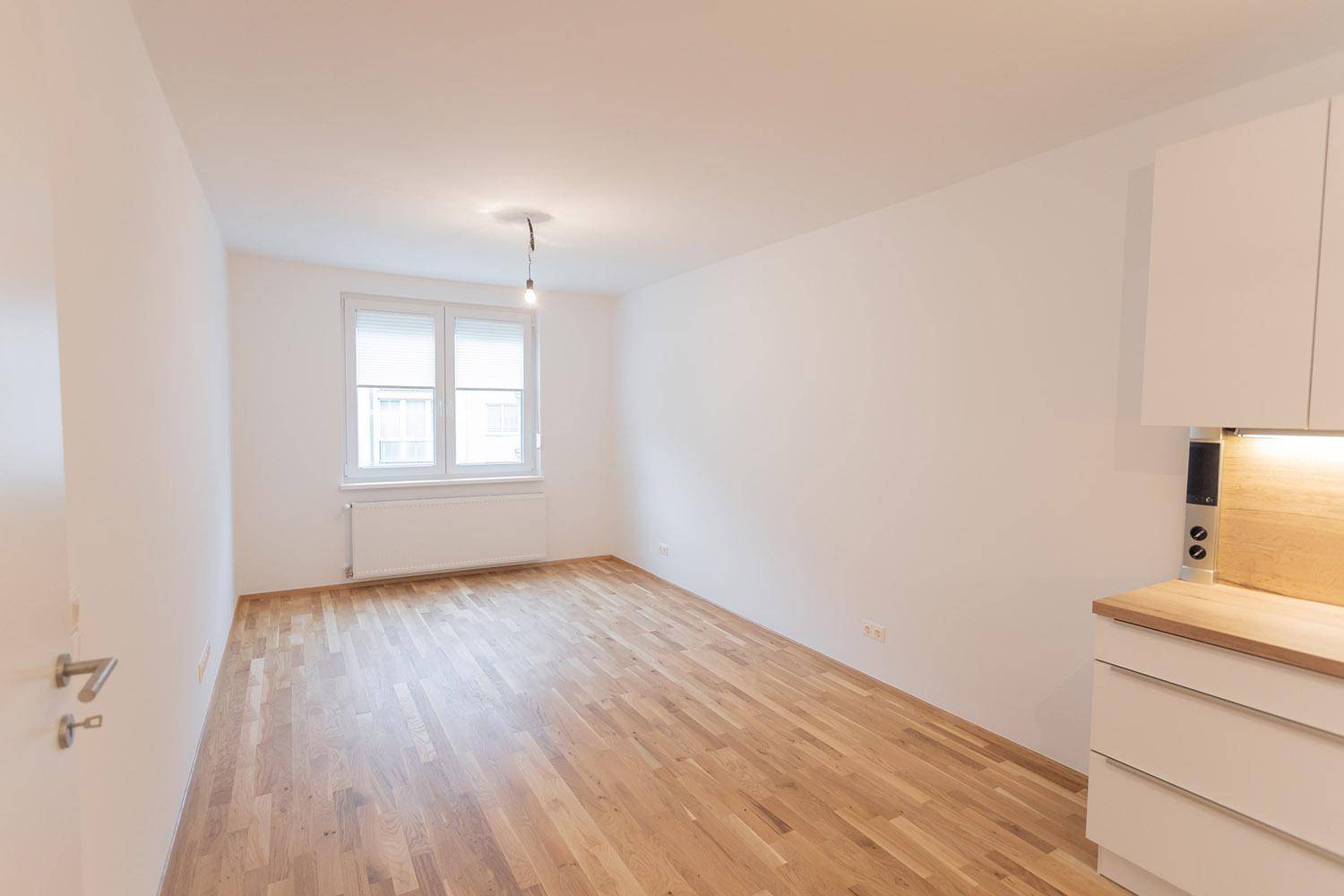 Heller Wohnbereich mit Holzboden und Fenster, angrenzend an die Küchenzeile.