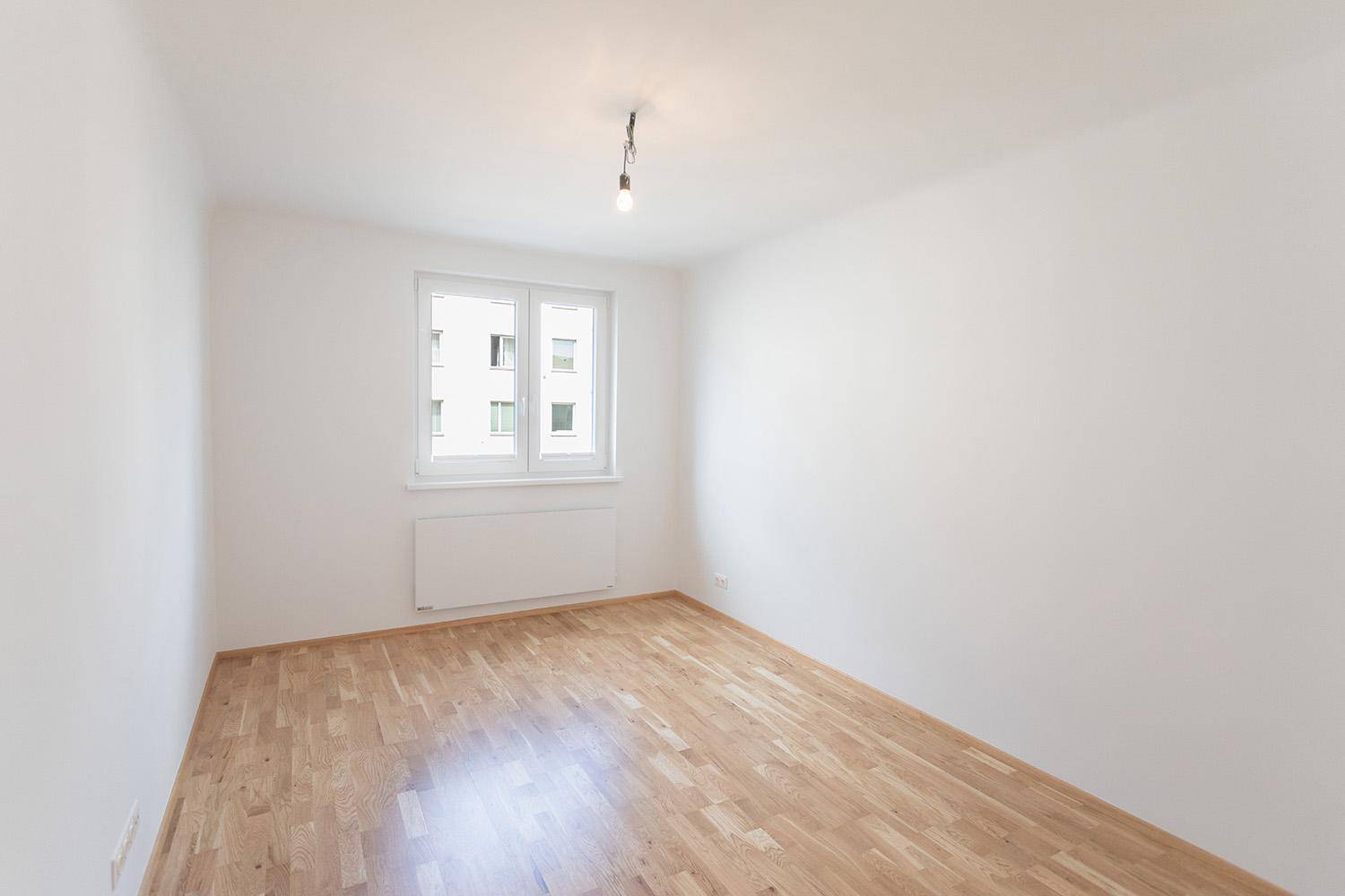 Helles Schlafzimmer mit Parkettboden und großem Fenster, unmöbliert und bezugsfertig.