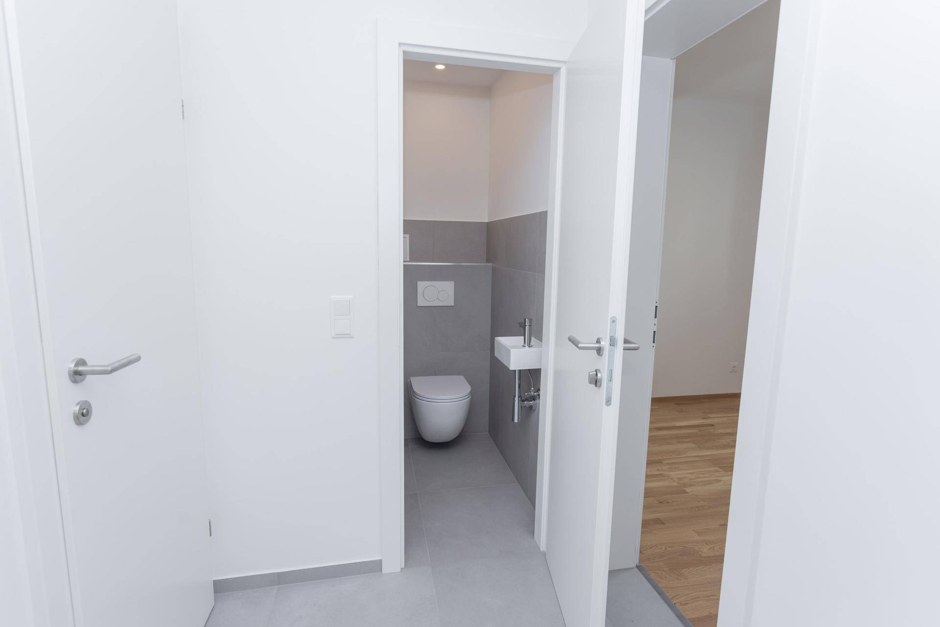 Modernes Gäste-WC mit wandhängender Toilette und kleinem Waschbecken, hell gefliest.
