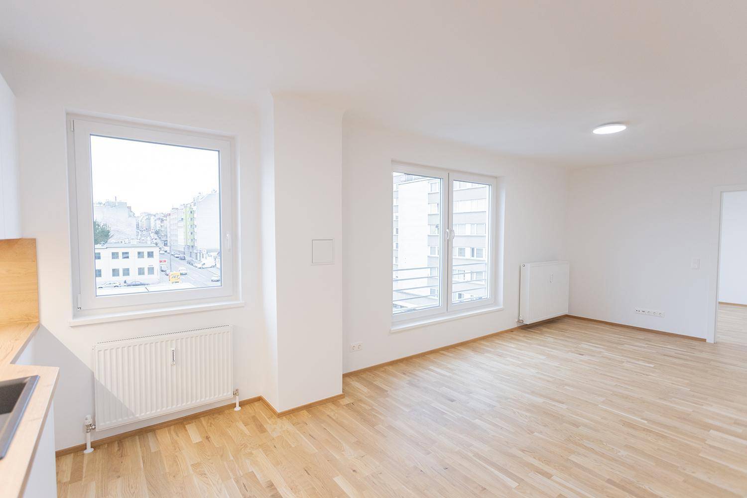 Heller Eckbereich mit Holzboden und zwei Fenstern, die einen Stadtblick ermöglichen.