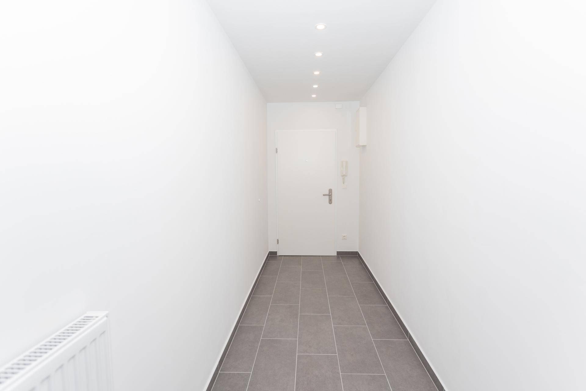 Heller Eingangsbereich mit modernen grauen Fliesen und Einbaustrahlern an der Decke.