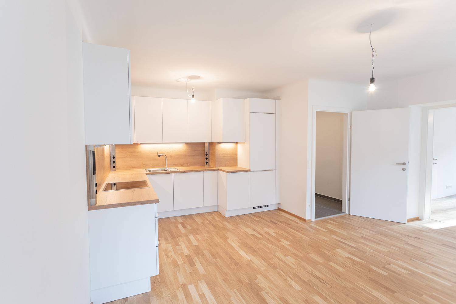 Funktionale Einbauküche mit weißen Schränken, Holzarbeitsplatten und integriertem Kühlschrank.