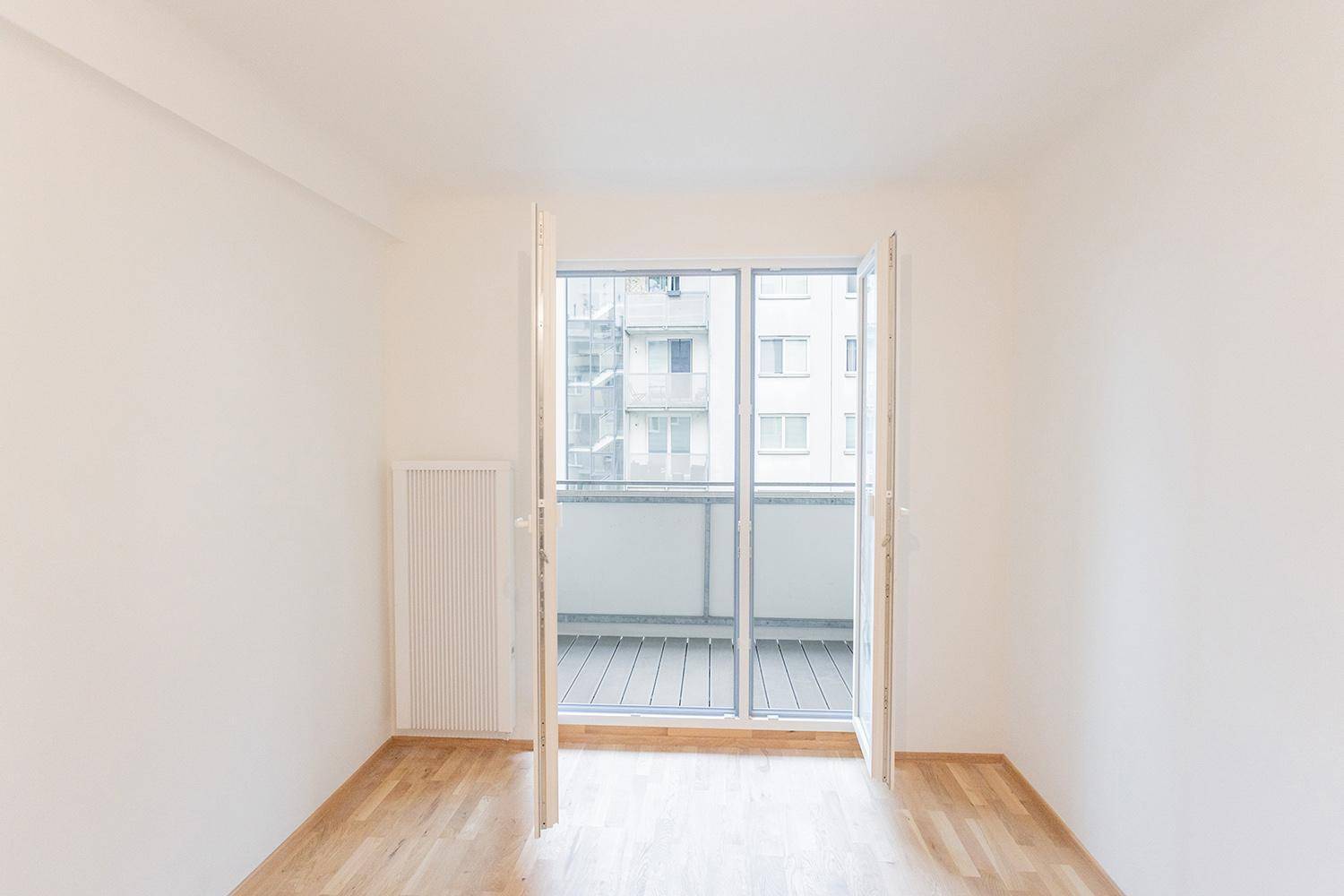 Heller Raum mit Parkettboden und weit geöffneten Balkontüren, die viel Tageslicht hereinlassen.