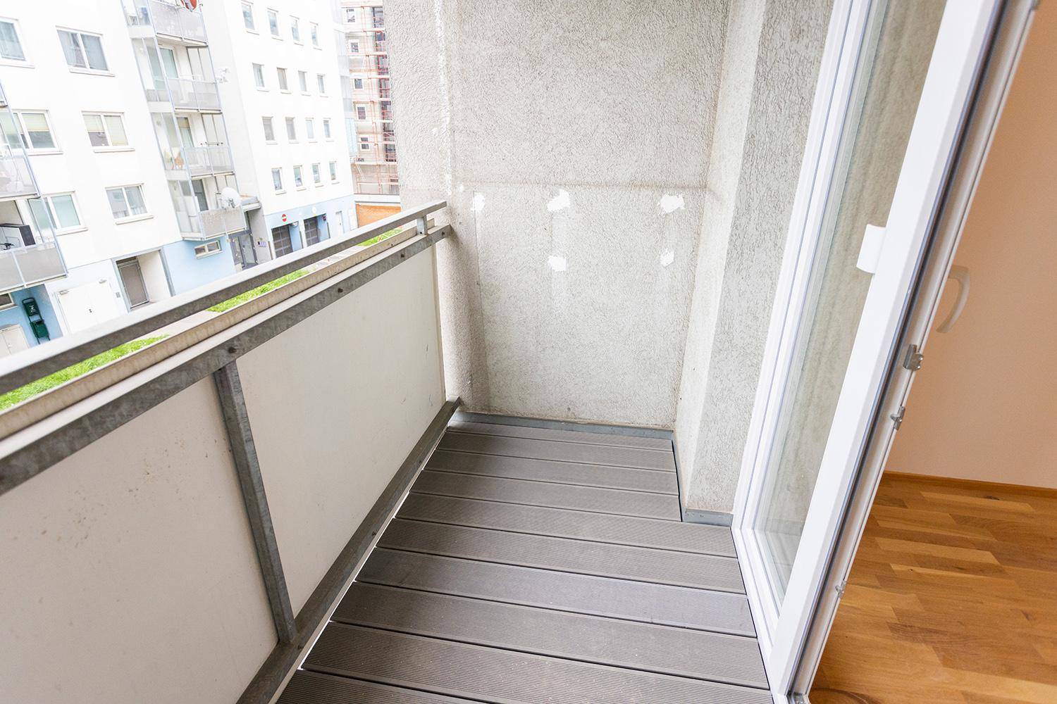 Schmaler Balkon mit grauem Dielenboden und Metallgeländer, bietet Platz für eine kleine Sitzecke.