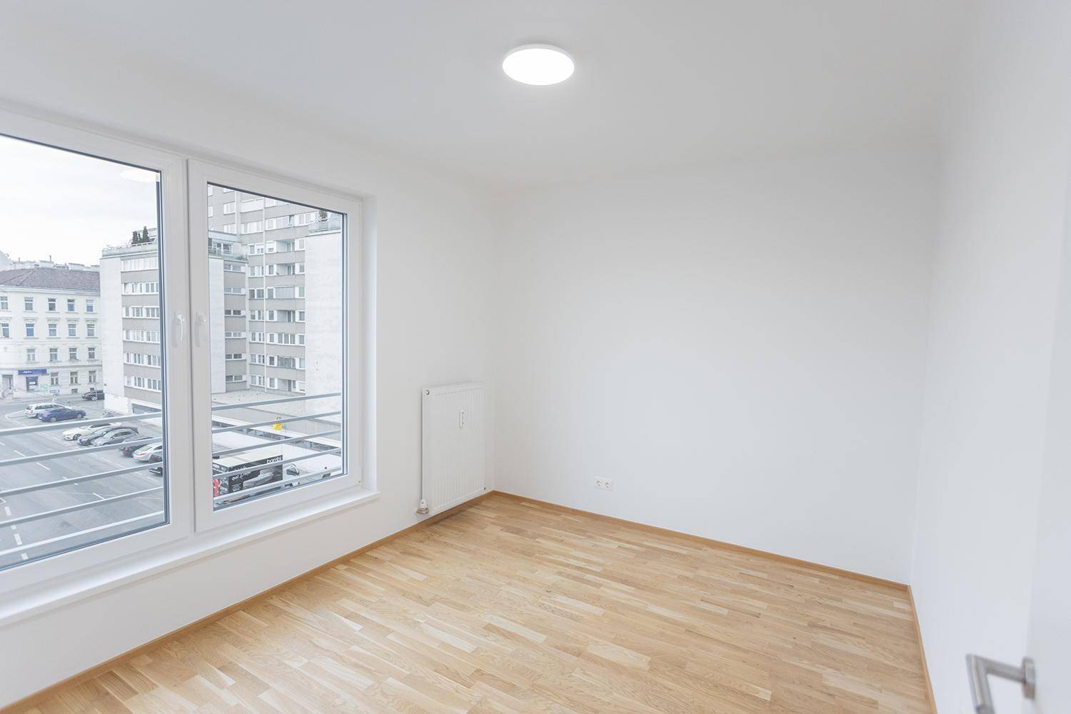 Heller Raum mit Holzboden und großem Fenster, das einen Blick auf die Stadt bietet.
