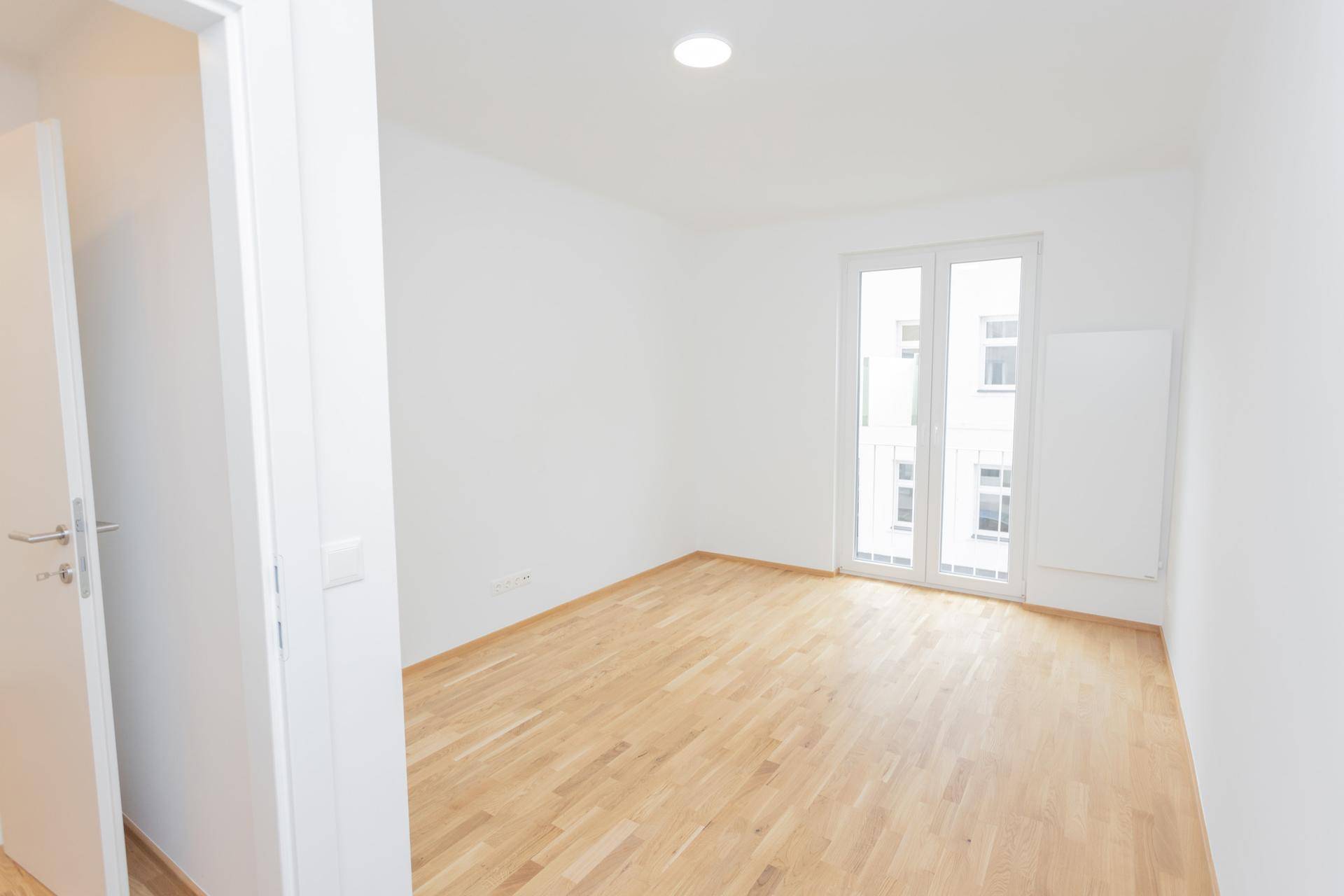 Heller, leerer Raum mit Holzfußboden und Zugang zu einem französischen Balkon.