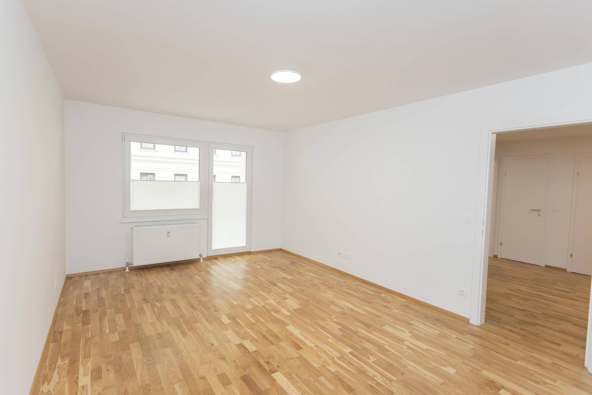 Geräumiges Zimmer mit Parkettboden und Fenster, das den Blick auf die Umgebung freigibt.