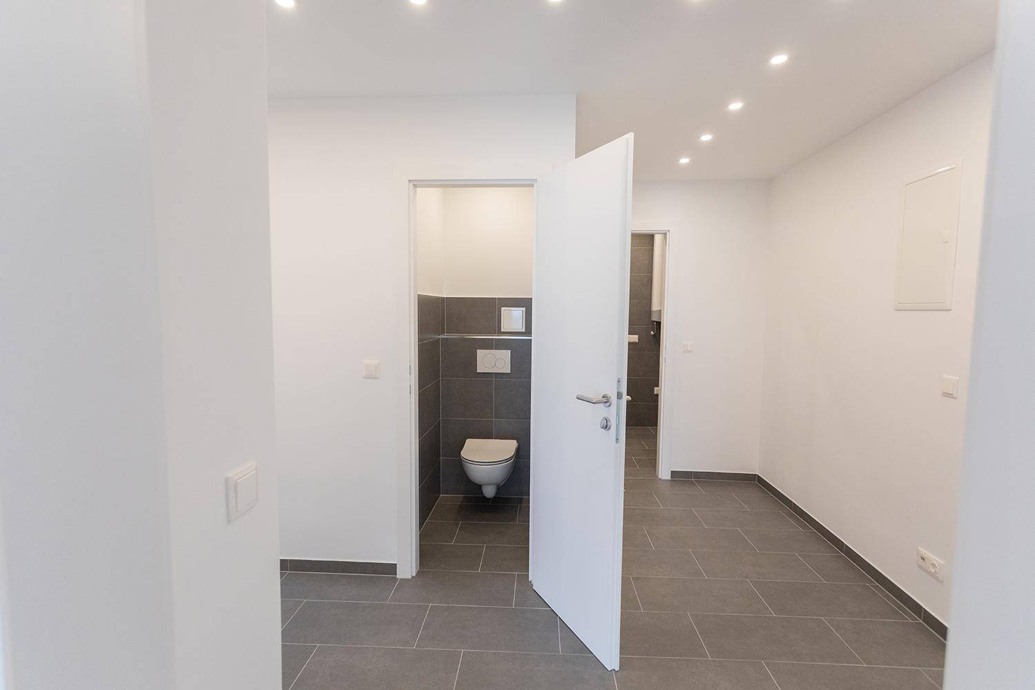 Separates WC mit wandhängender Toilette und modernen grauen Fliesen im Eingangsbereich.