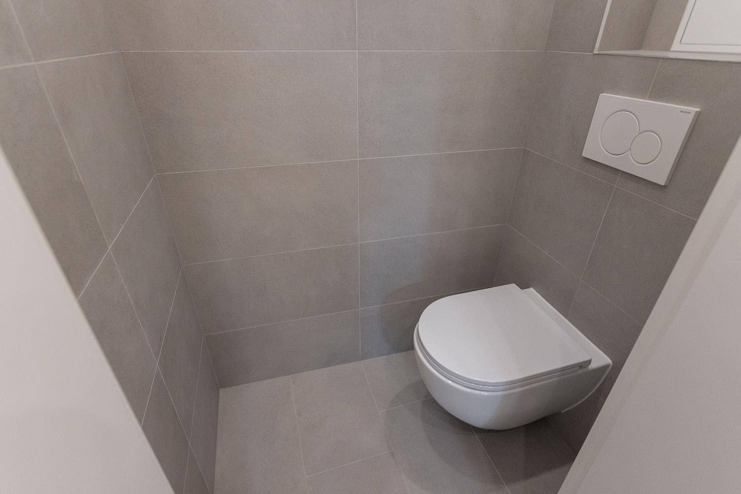 Moderne Gästetoilette mit grauen Fliesen und wandhängendem WC.