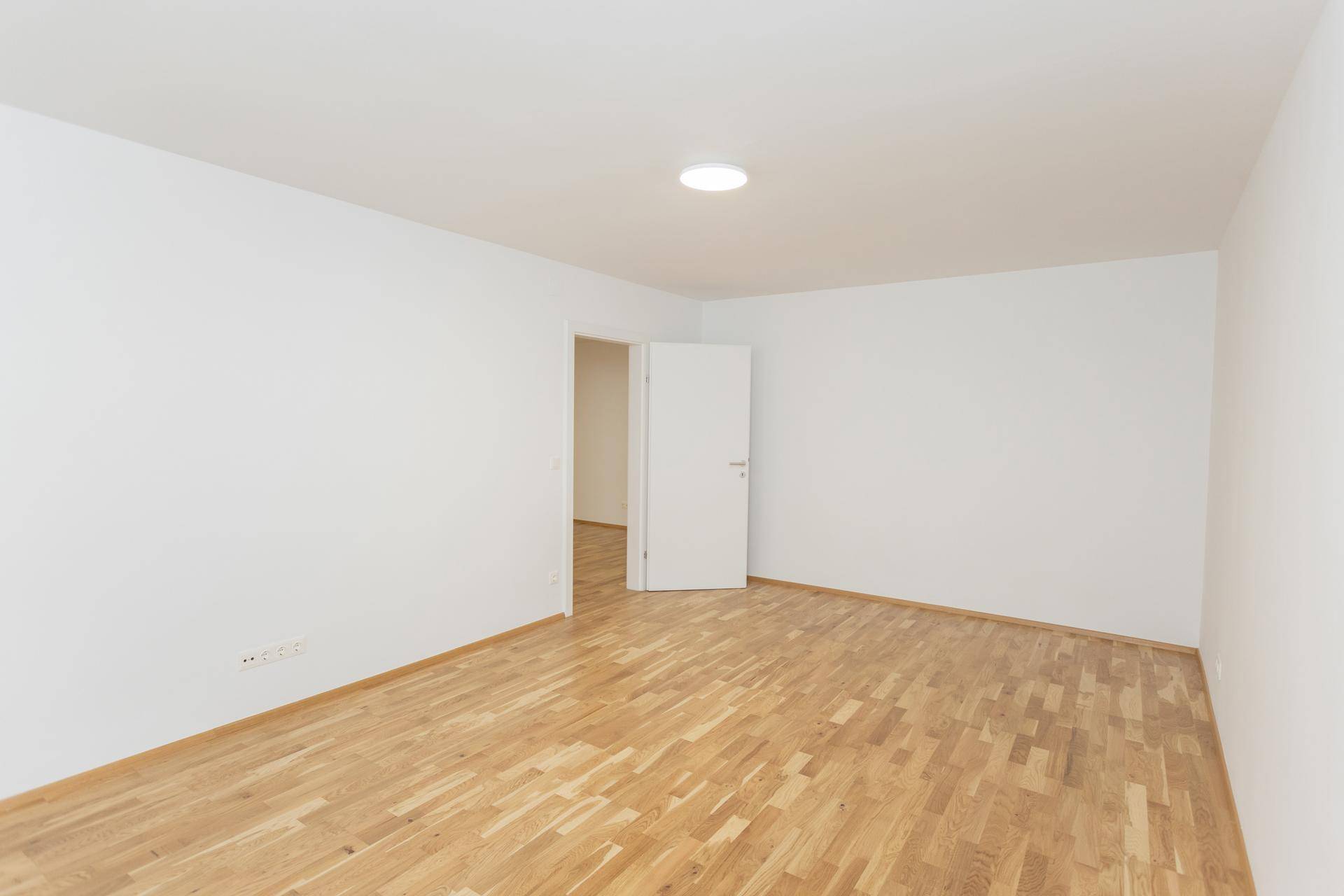 Leeres Zimmer mit Parkettboden und offener Tür, bereit für die individuelle Gestaltung.