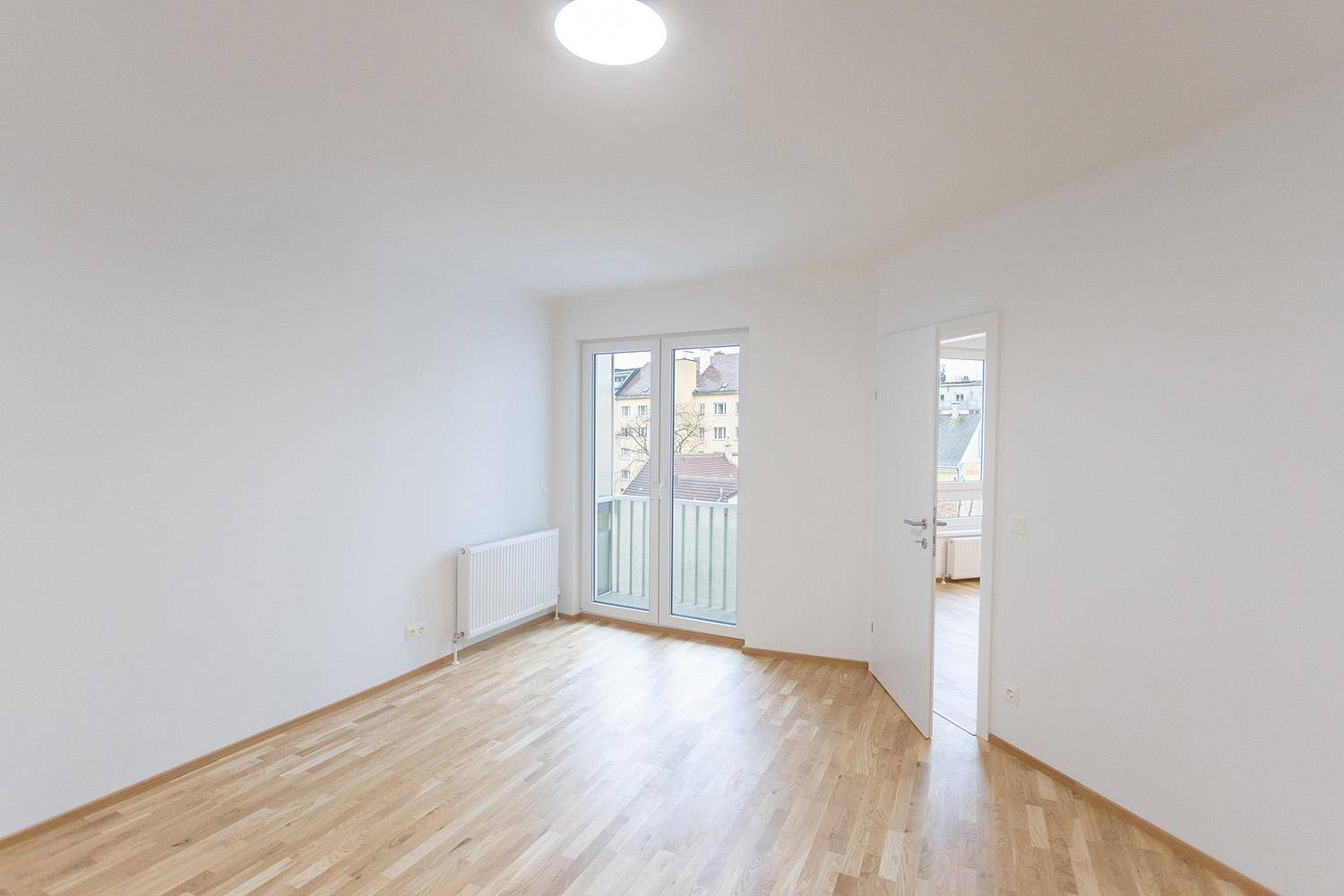 Helles Schlafzimmer mit Holzboden, Heizkörper und Zugang zu einem französischen Balkon.