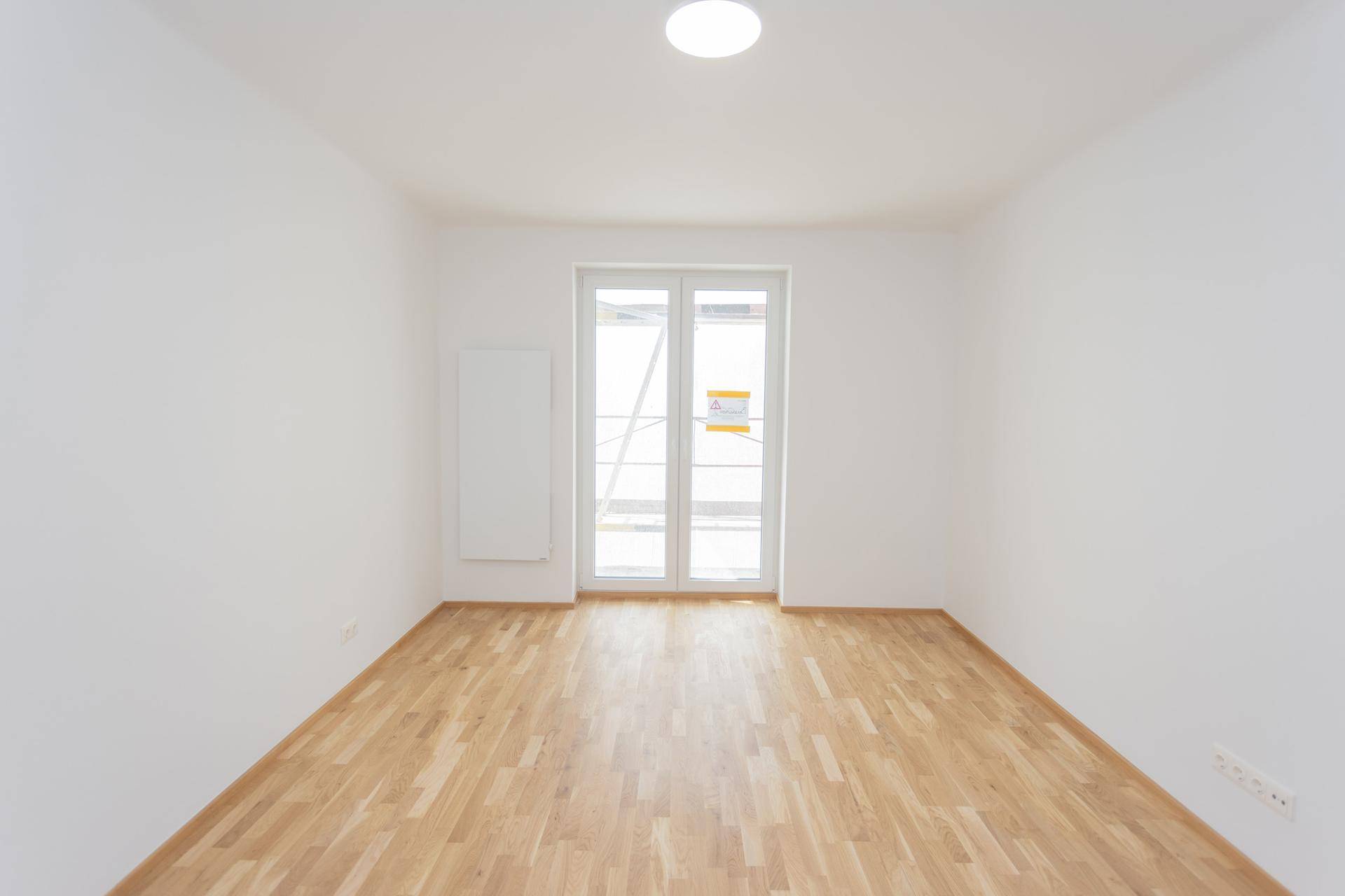 Helles Zimmer mit Parkettboden und großen Fenstertüren zum zukünftigen Balkon.
