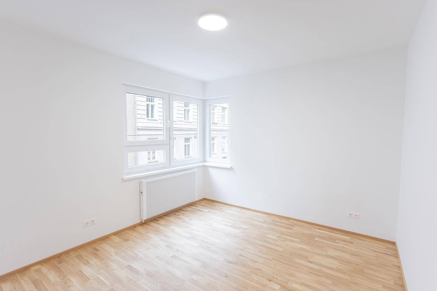 Leeres Schlafzimmer mit Holzparkettboden und großen Fenstern, das viel Tageslicht bietet.