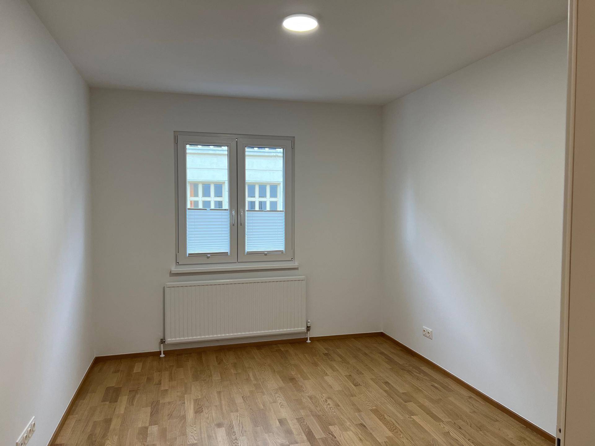 Leeres Zimmer mit hellem Holzboden, weiß gestrichenen Wänden und Fenster mit Ausblick.