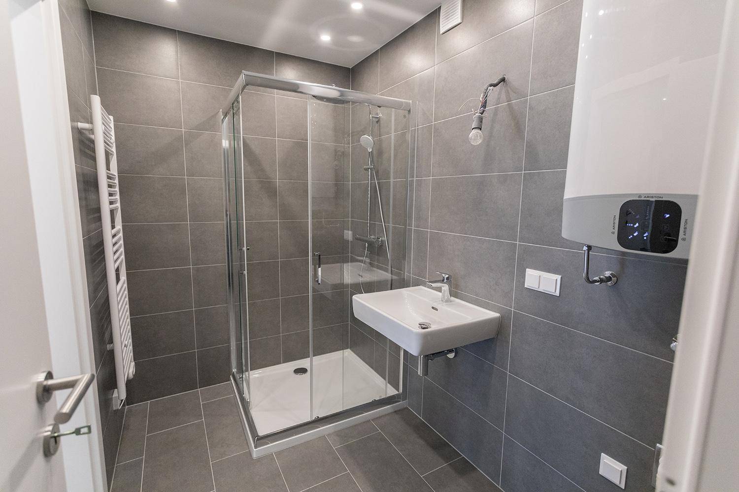 Modernes Badezimmer mit grauen Fliesen, Duschkabine und beheiztem Handtuchhalter.