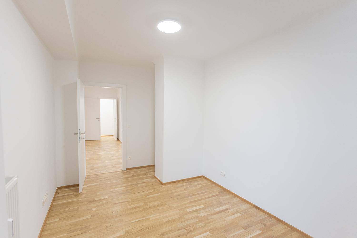 Leerer Raum mit Parkettboden und Zugang zu einem weiteren Zimmer, hell und funktional.