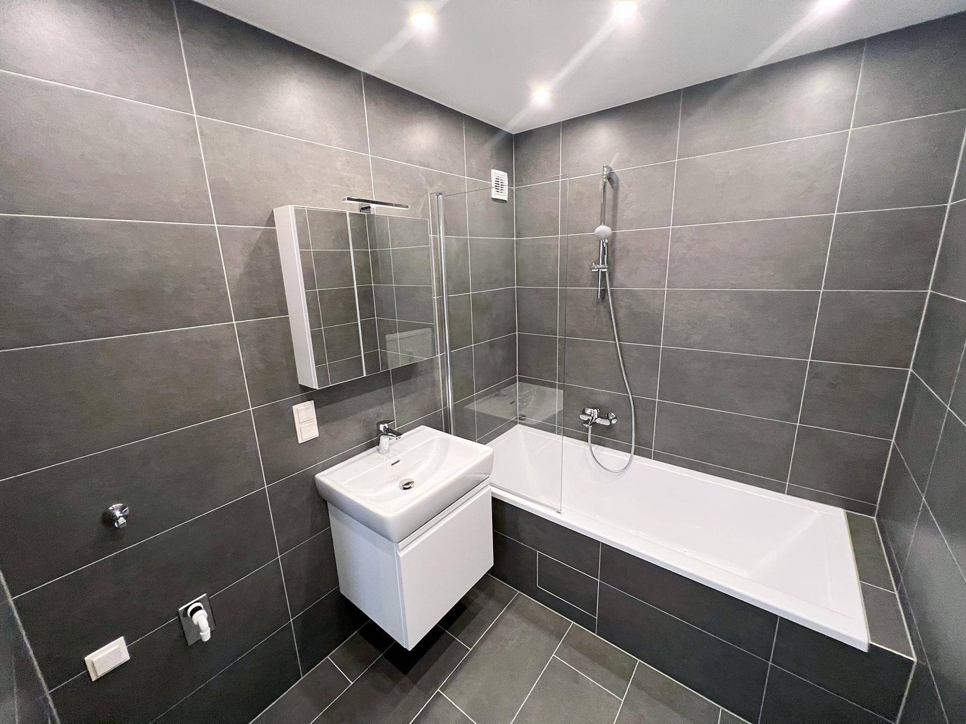 Modernes Badezimmer mit dunklen Fliesen, Badewanne mit Duschfunktion und elegantem Waschtisch.
