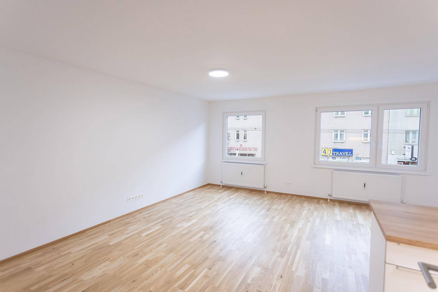 Geräumiger, unmöblierter Wohnbereich mit hellem Parkettboden und zwei großen Fenstern.