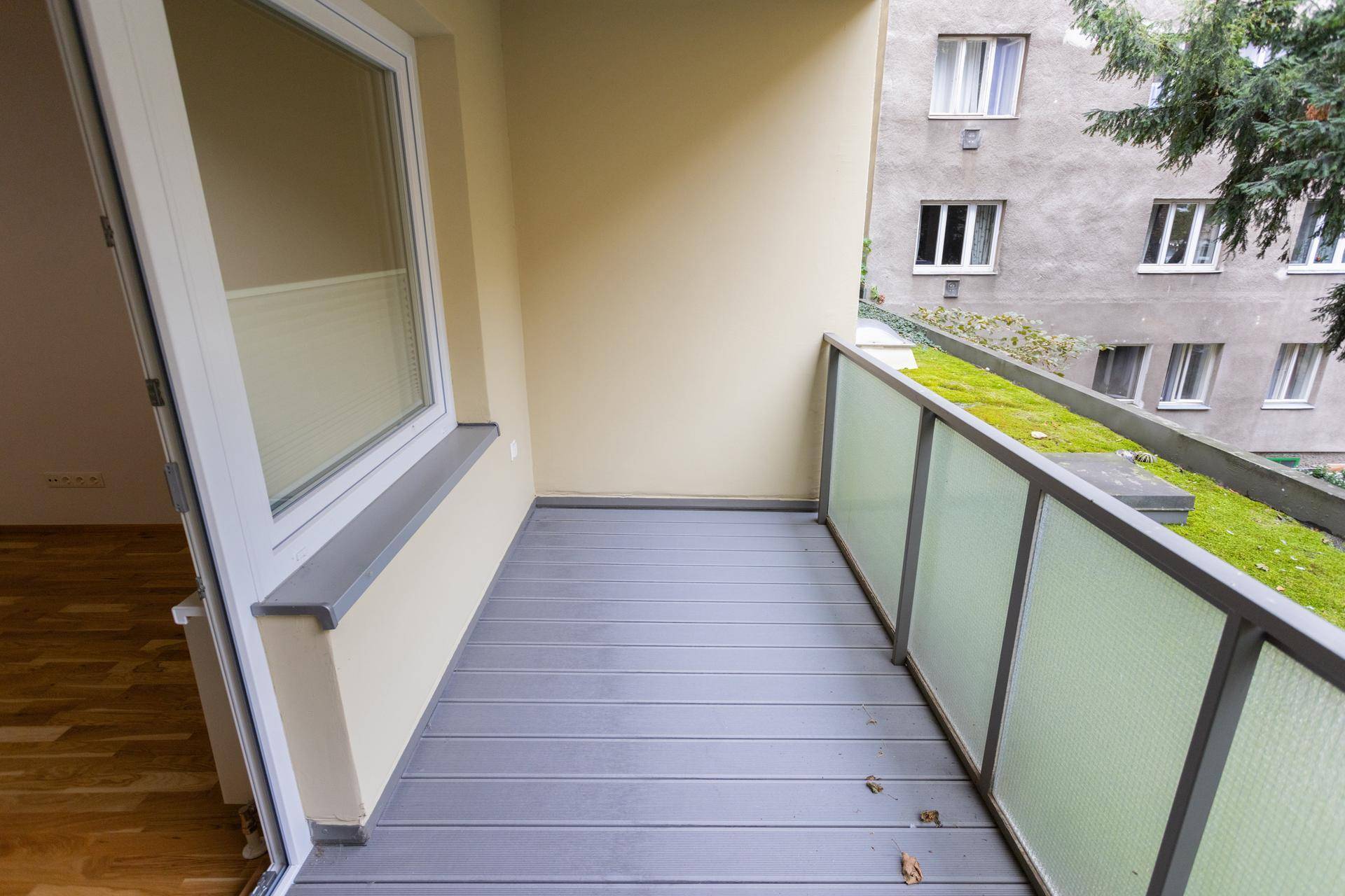 Heller Balkon mit modernem Bodenbelag und Ausblick auf eine begrünte Umgebung.