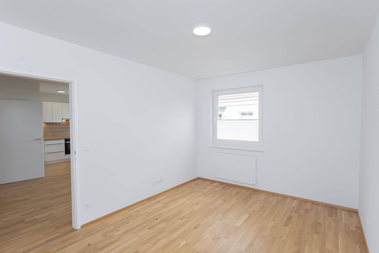 Helles Schlafzimmer mit Eichenparkett und großem Fenster, bietet viel Tageslicht.
