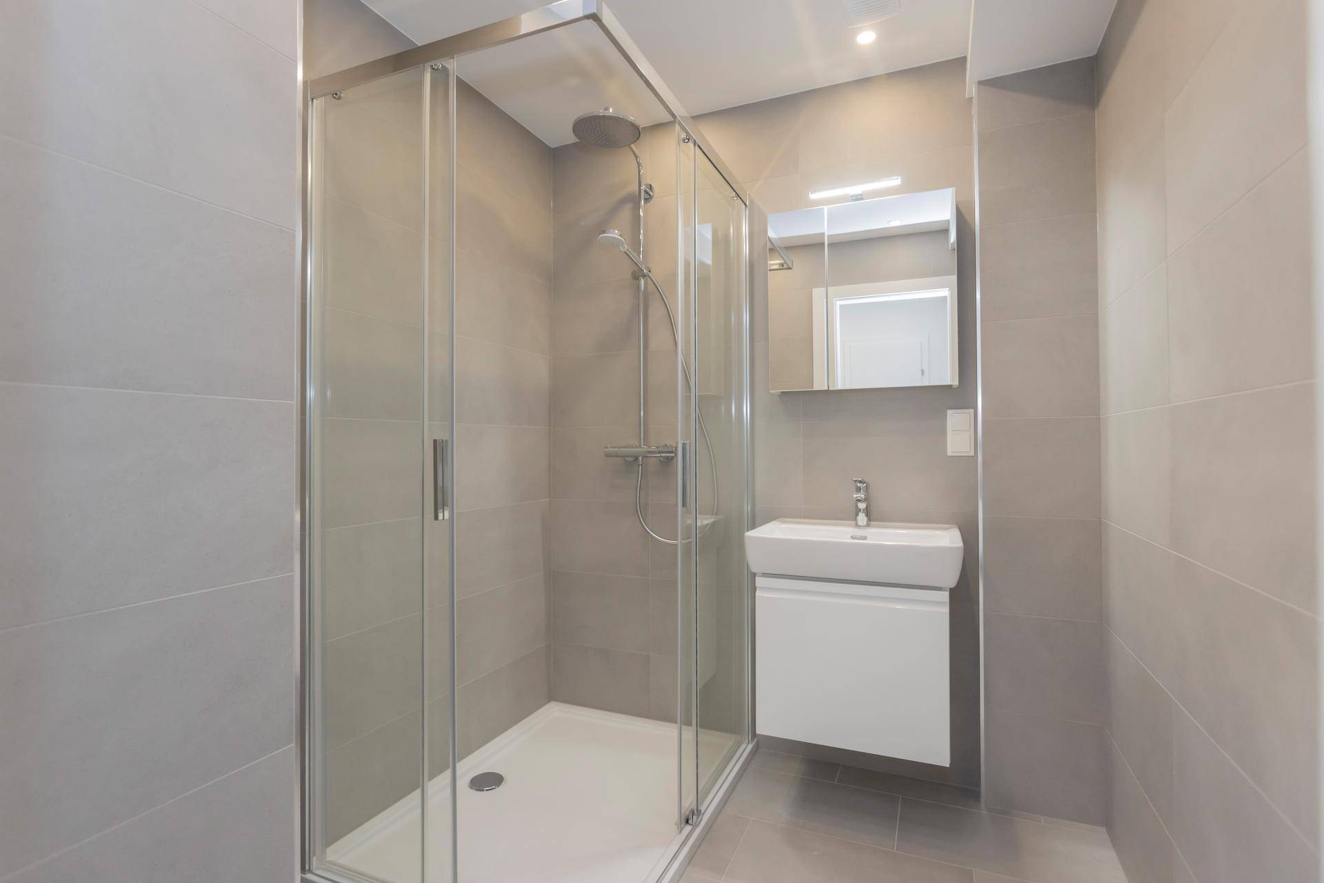 Modernes Badezimmer mit Duschkabine, Waschbecken und hellgrauen Wand- und Bodenfliesen.