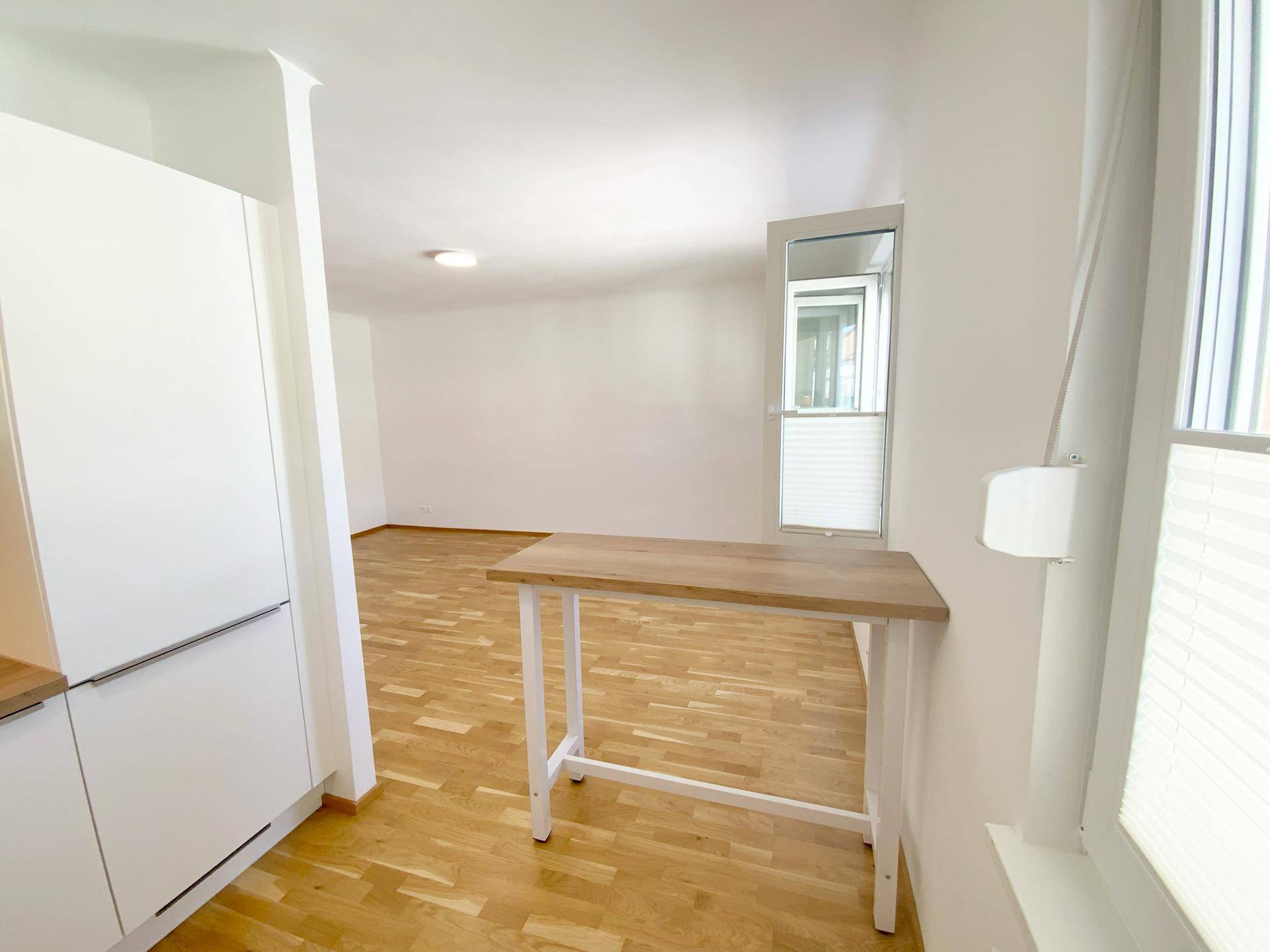 Blick von der Küche in den Wohnbereich mit einer kleinen Frühstückstheke und Parkettboden.