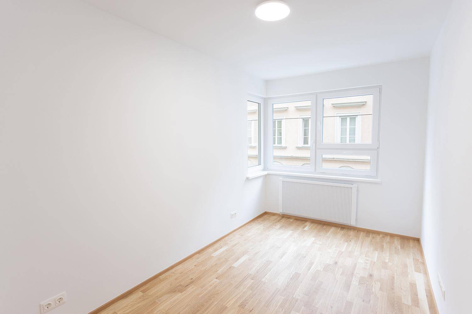Heller Raum mit Holzparkettboden und großen Fenstern, ideal als Schlaf- oder Kinderzimmer.